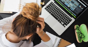 Girl leaning over laptop, papers on her desk, head in her hands from frustration